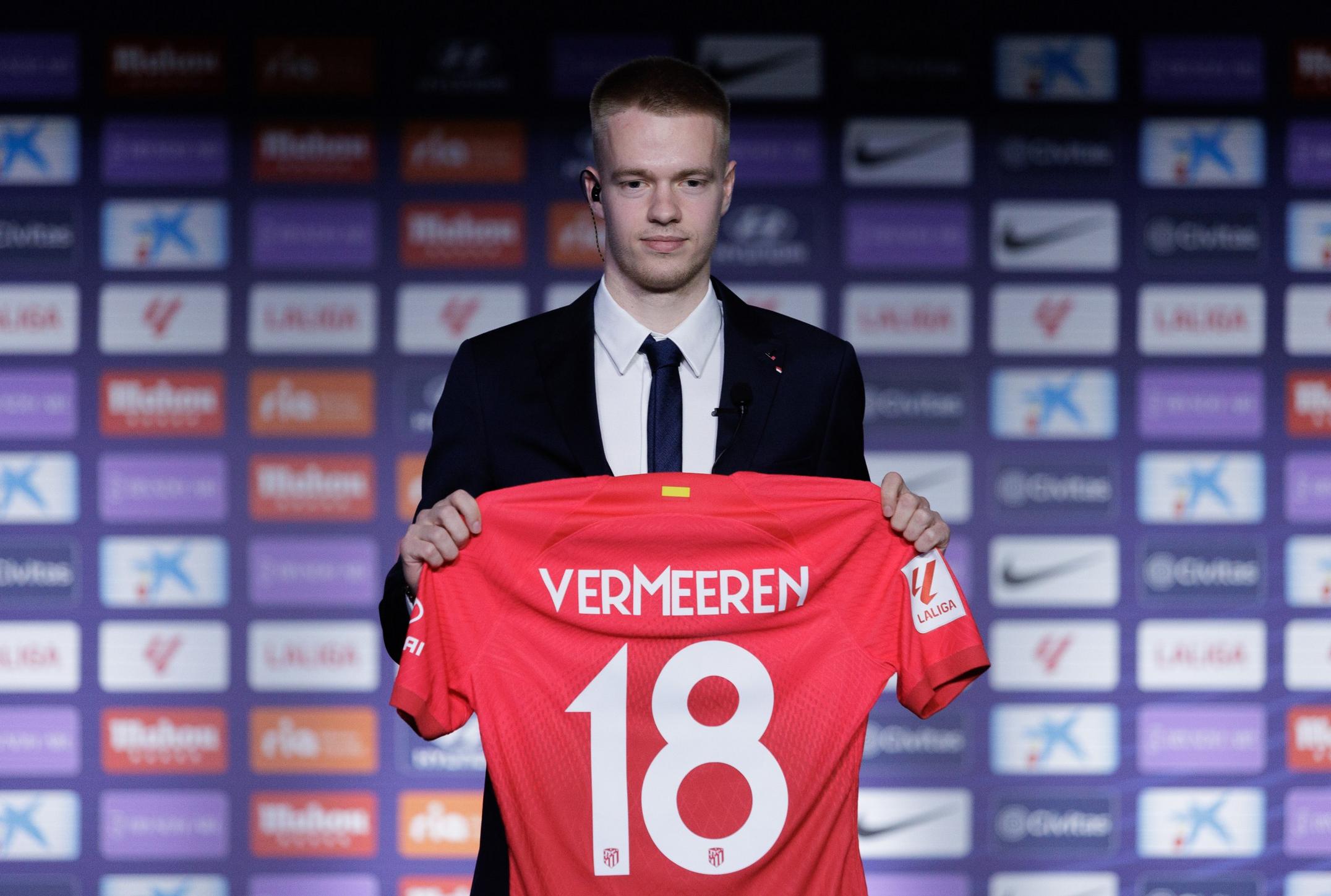 Arthur Vermeeren holding a red jersey with 'VERMEEREN' and number 18 at a press event.