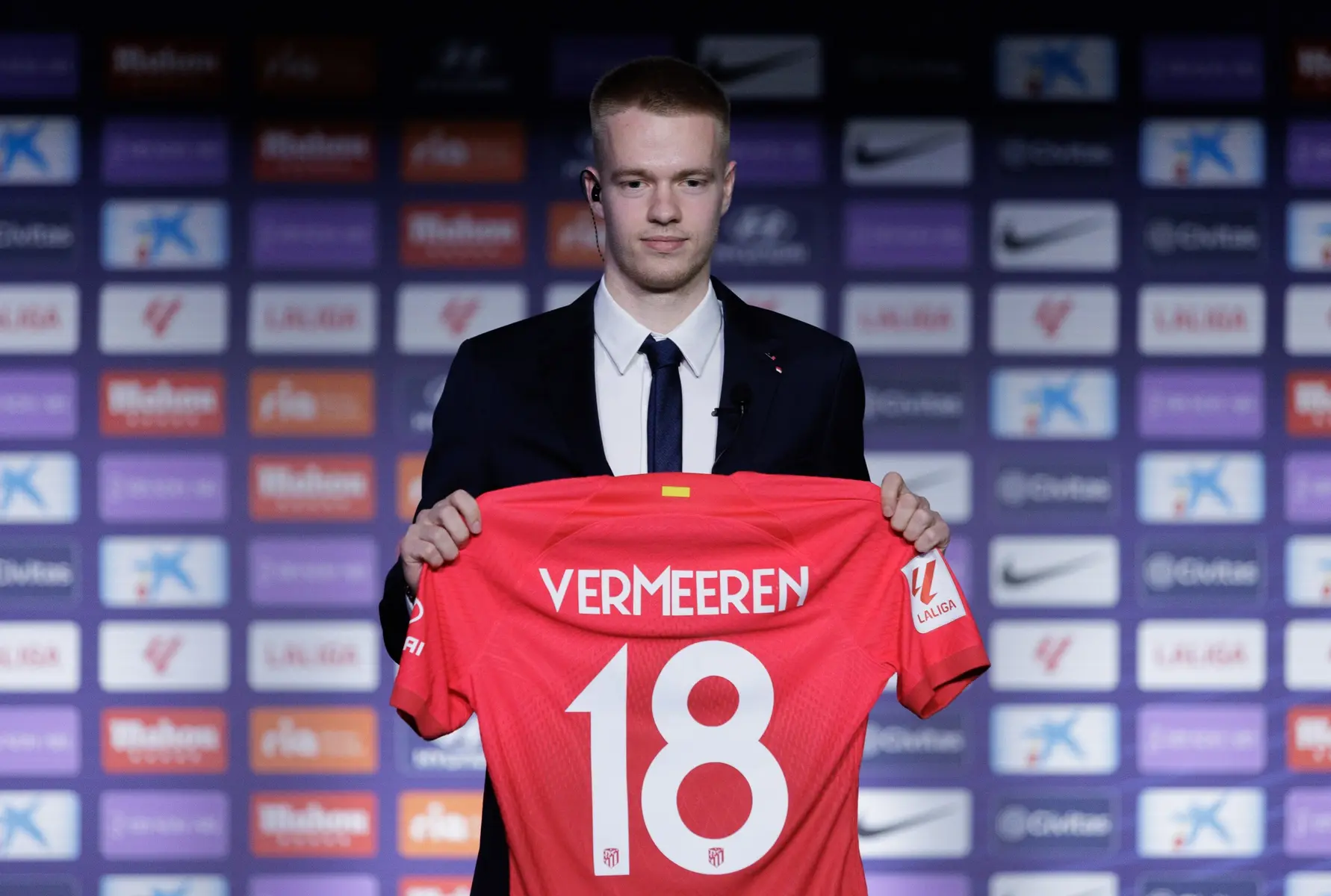 A young man in a suit holds a red football jersey with 'VERMEEREN' and the number '18'.