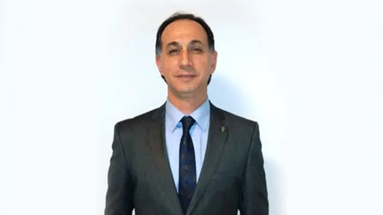 A man in a suit and tie, standing against a plain backdrop.