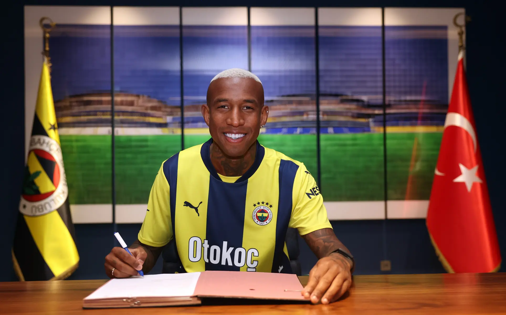 Anderson Talisca wearing a Fenerbahçe jersey while signing a contract at a desk