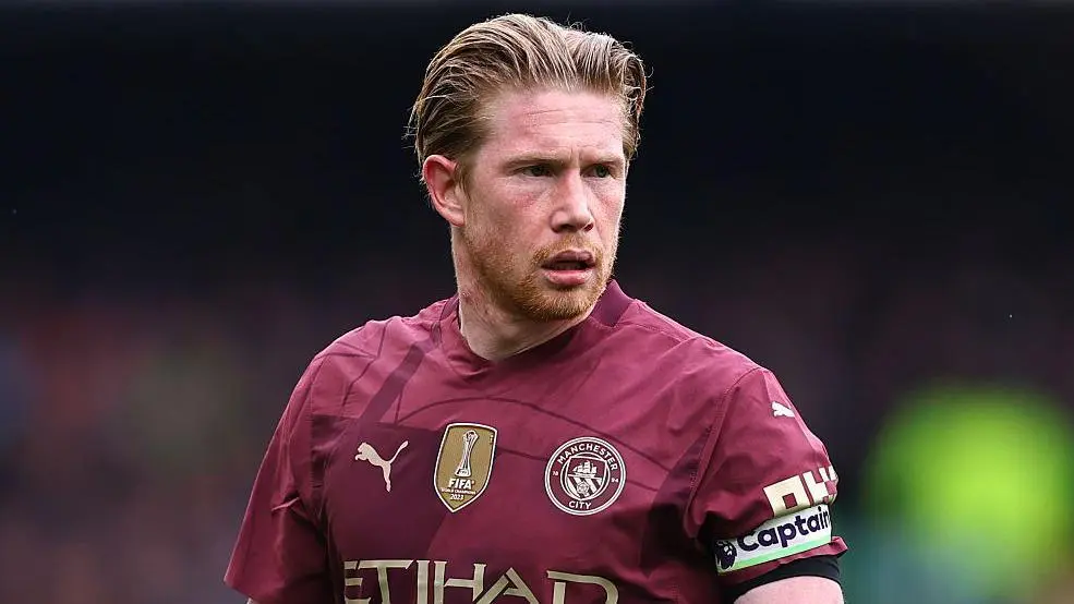 Close-up portrait of Kevin De Bruyne wearing a maroon Manchester City jersey with the captain's armband.