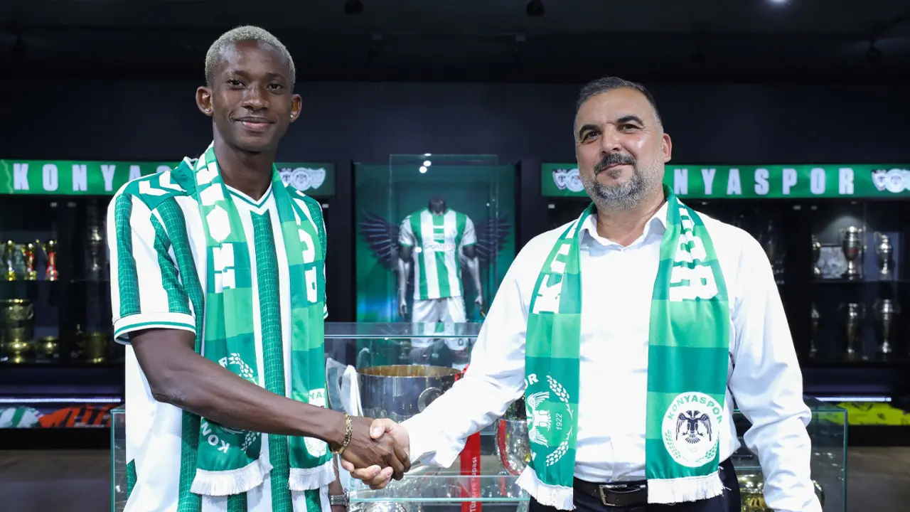 A football player in a Konyaspor kit and a club official shaking hands at a signing ceremony.