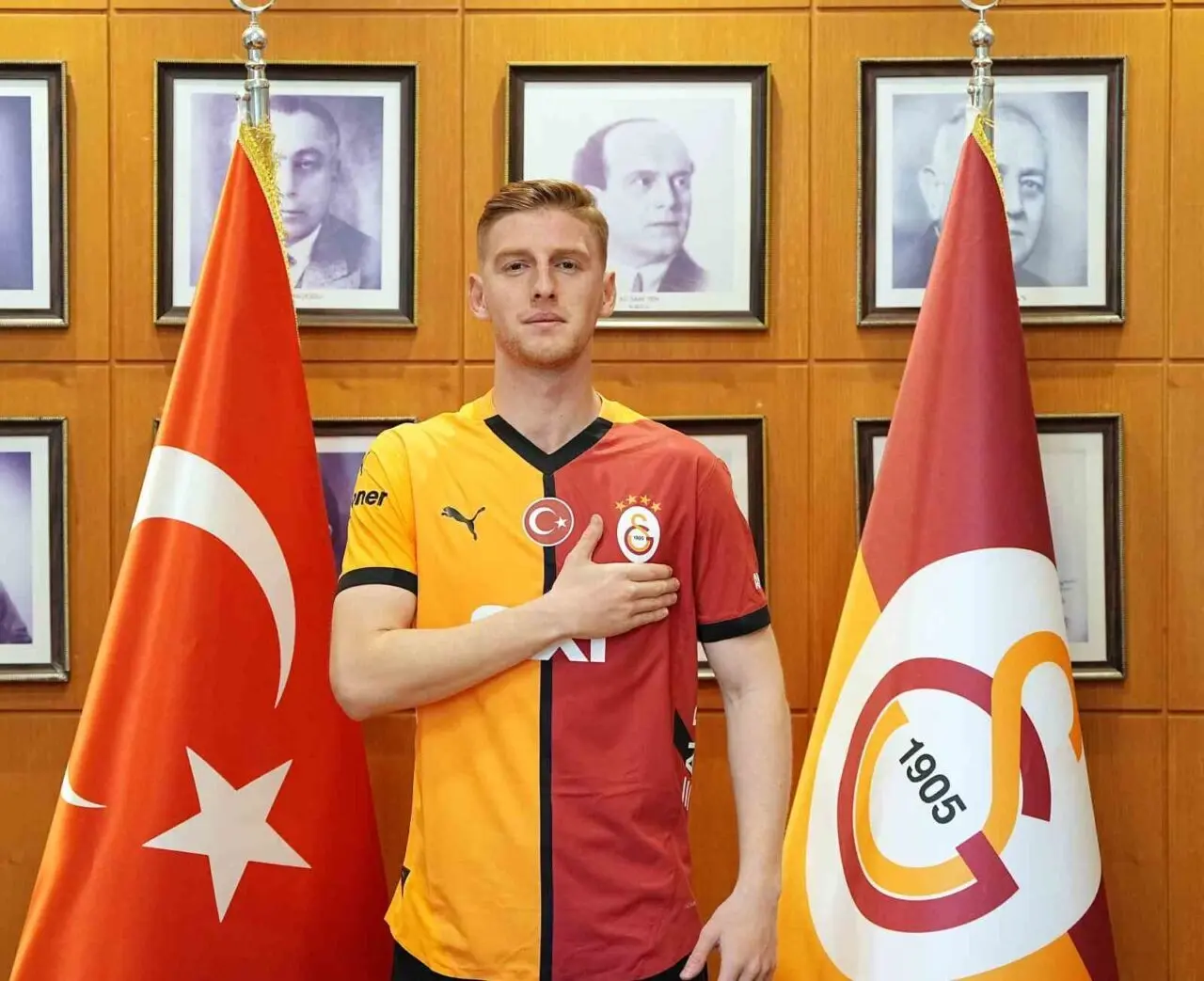 Metehan Baltacı posing in a Galatasaray jersey between the Turkish flag and the club flag