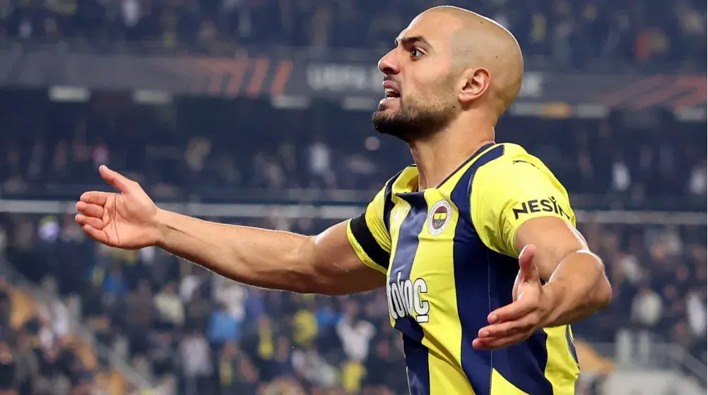 Sofyan Amrabat in a yellow and navy blue Fenerbahçe jersey gesturing on the field