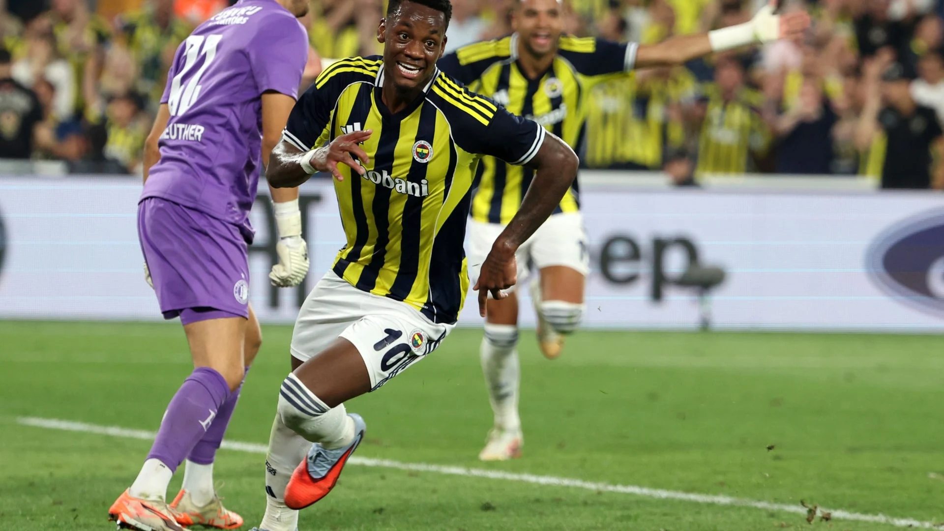 Sarı lacivert çubuklu formasıyla Fenerbahçe futbolcusu sahada koşuyor.